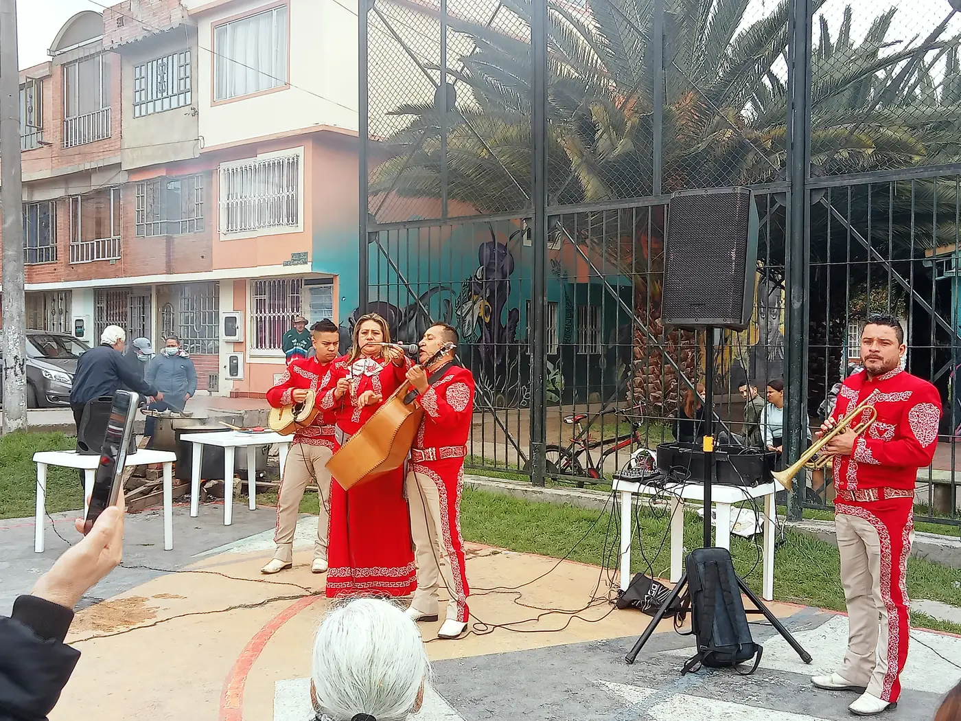 Trío de mariachis con traje rojo tocando en la cancha del barrio durante la celebración del Día de la Madre.