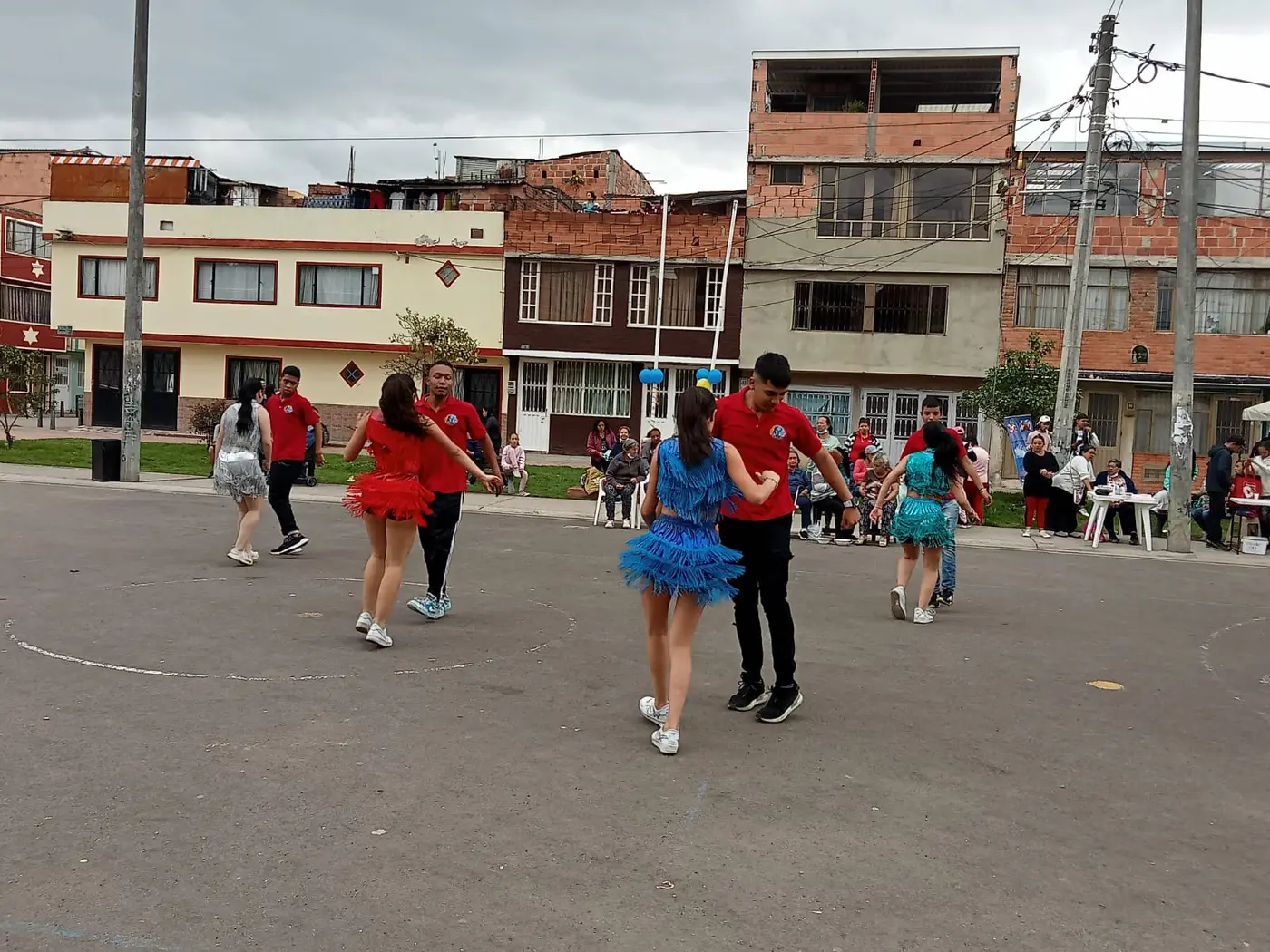 Parejas de bailarines con vestidos de volantes rojos y azules durante una presentación en la cancha del barrio.