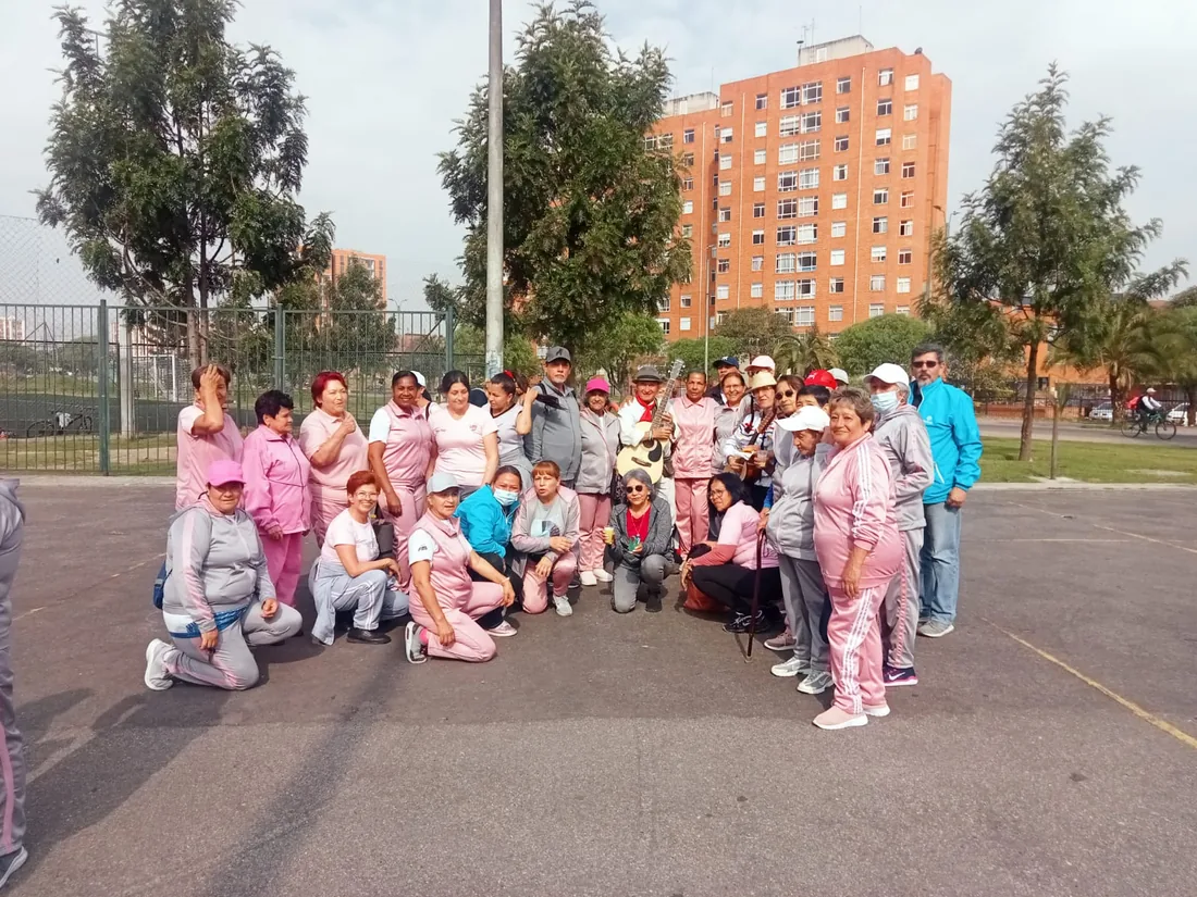 Grupo numeroso de personas mayores con sudaderas rosadas y grises de la fundación, reunidas en una cancha del barrio.